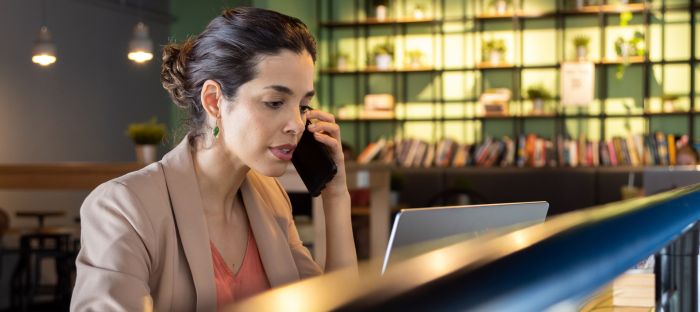 Woman using laptop while on phone in a cafe